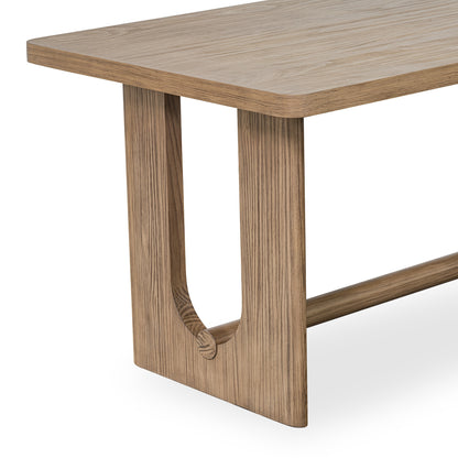 Modern wooden table with a rectangular top and unique U-shaped plinth legs connected by a horizontal support beam.