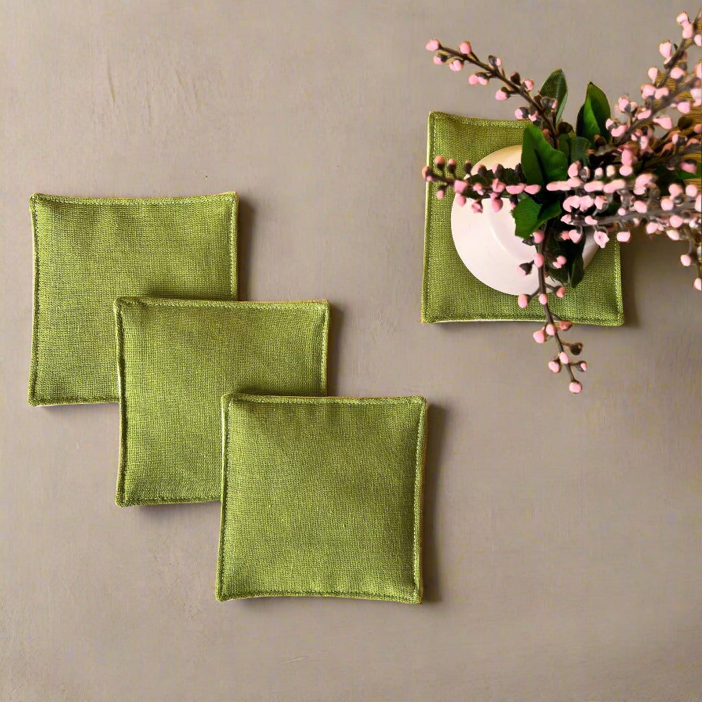 Green square coasters on a wooden surface with a decorative branch.